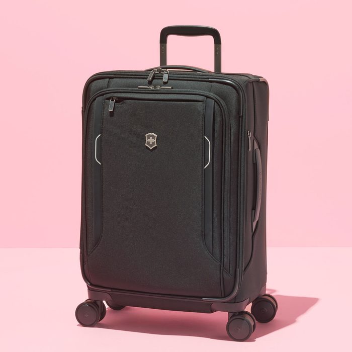 Suitcase stands on wheels against a pink background, featuring a retractable handle and a logo on the front pocket.