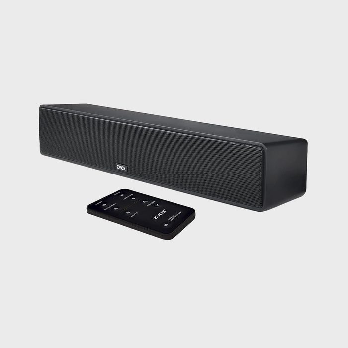 Soundbar sits on a plain surface, accompanied by a remote, in a minimalist setting. 
