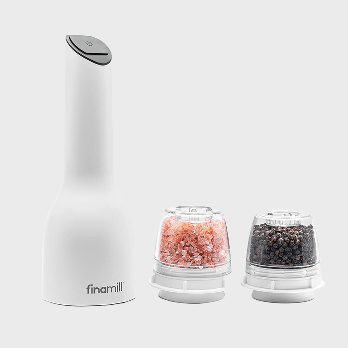 Electric spice grinder with interchangeable pods containing pink salt and peppercorns, resting on a neutral gray background.