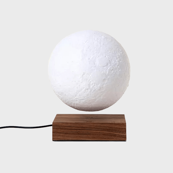 A textured white sphere levitates above a wooden base, connected by a black power cord, against a plain gray background.
