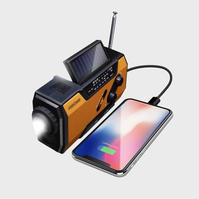 A yellow emergency radio charges a nearby smartphone; the radio features a solar panel, flashlight, and antenna, on a plain gray background.