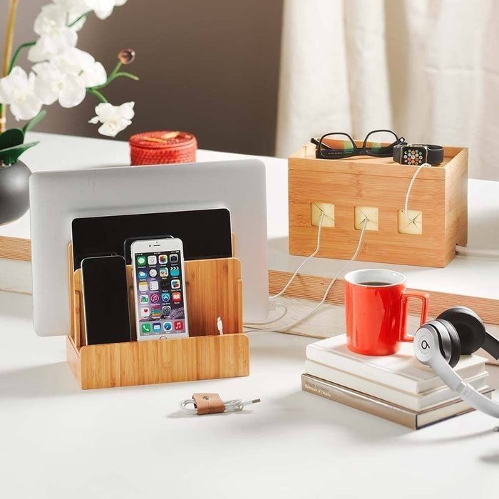 Wooden organizers hold devices and accessories; one contains a tablet, smartphones, and cables, while another holds sunglasses and a watch, on a clean desk.