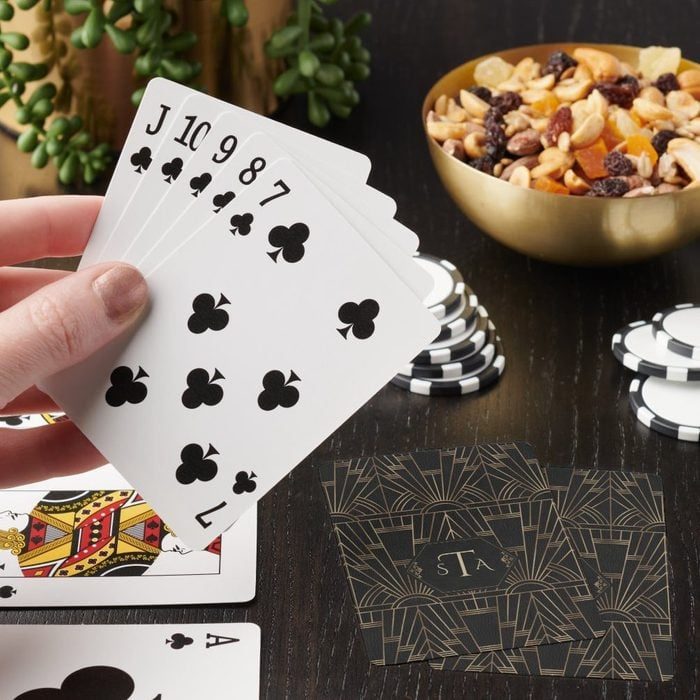 Hand holds playing cards, showing a straight flush, near poker chips and a bowl of mixed nuts on a dark table.