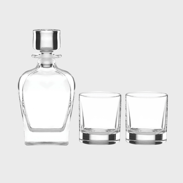 A clear glass decanter stands beside two empty glasses on a plain background.