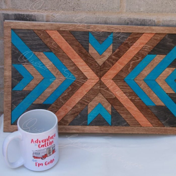 Wooden geometric artwork with blue and brown chevron patterns is displayed against a brick wall. A mug reads, 