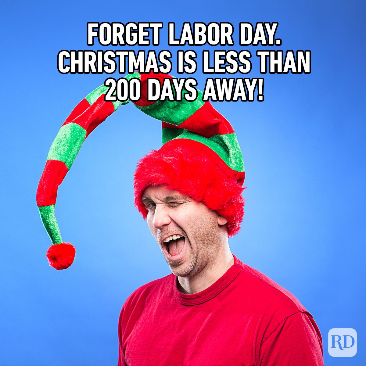 Man grinning in red shirt and festive hat against a blue background. Text reads: "FORGET LABOR DAY. CHRISTMAS IS LESS THAN 200 DAYS AWAY!"
