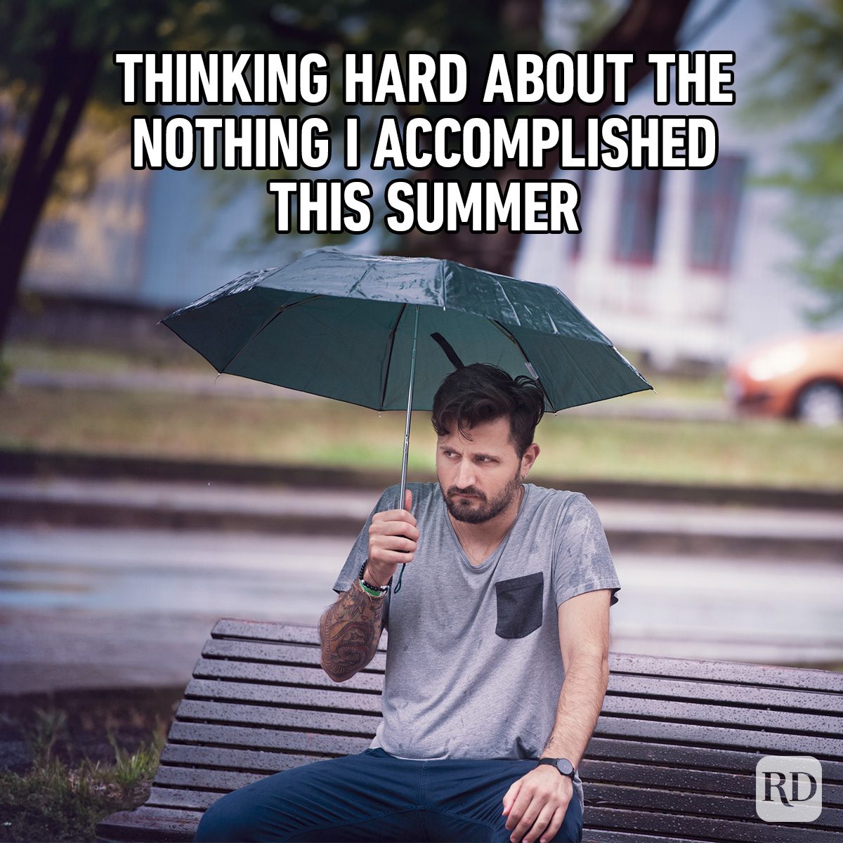 Man sits holding an umbrella, looking thoughtful on a rainy park bench. Text reads: "THINKING HARD ABOUT THE NOTHING I ACCOMPLISHED THIS SUMMER."