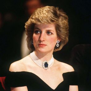 A woman with short, styled hair looks aside, wearing a pearl necklace with a blue gem and matching earrings, in an elegant setting.