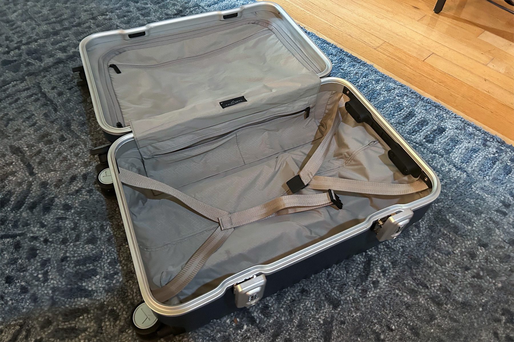 Open suitcase with straps, sitting on a textured blue carpet in a room with wooden flooring.