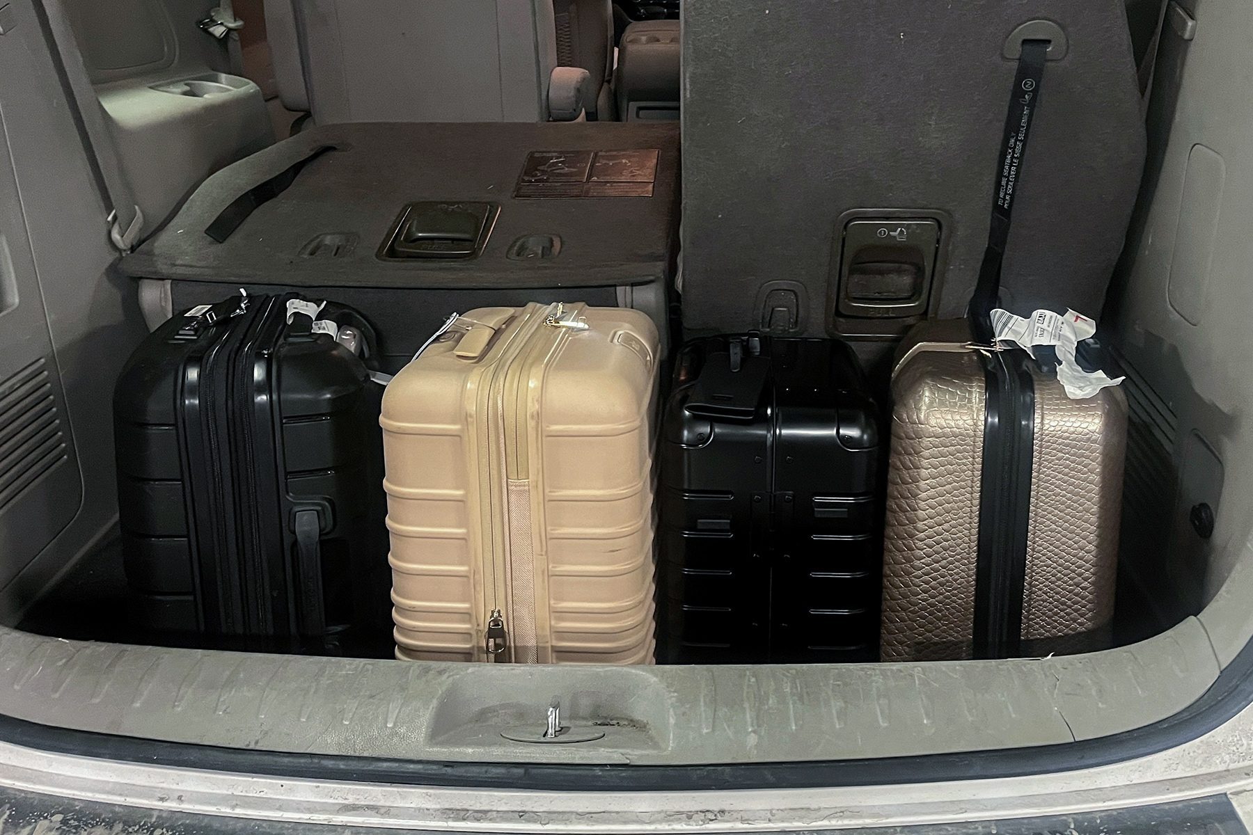 Four suitcases are neatly arranged inside a car trunk, surrounded by a dark interior and folded back seats.