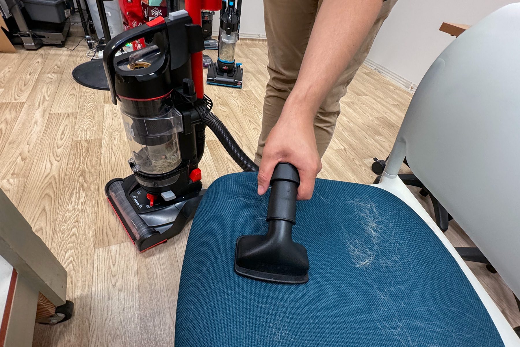 Vacuum cleaner removes pet hair from a blue chair in a room with light wood flooring.