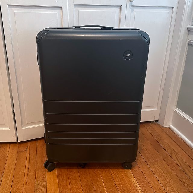 A black suitcase stands upright on wooden floor, near white-paneled closet doors.
