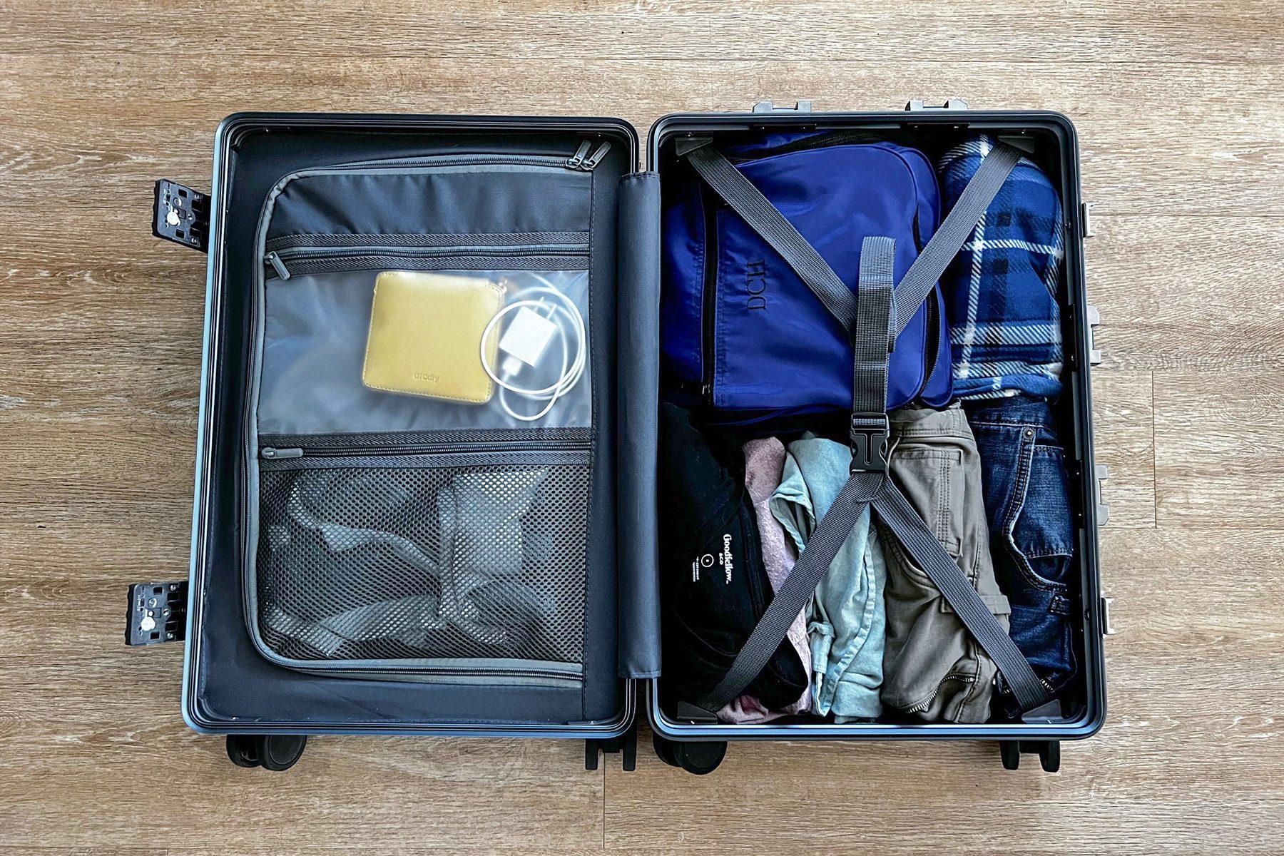 Suitcase lies open, displaying neatly packed clothes and accessories in compartments, on a wooden floor.