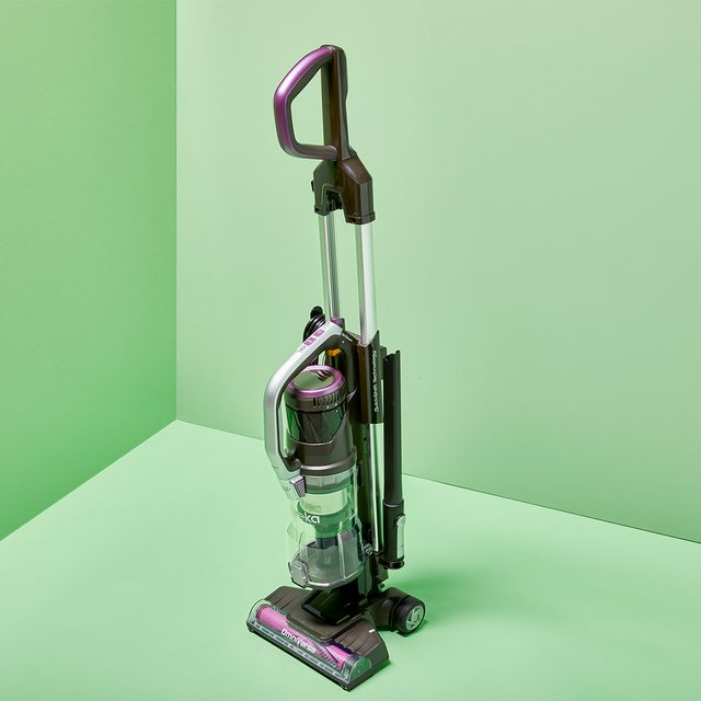 Vacuum cleaner stands upright on a solid light green background.