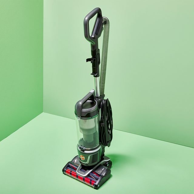 Vacuum cleaner stands upright, with hose coiled, on a light green background.