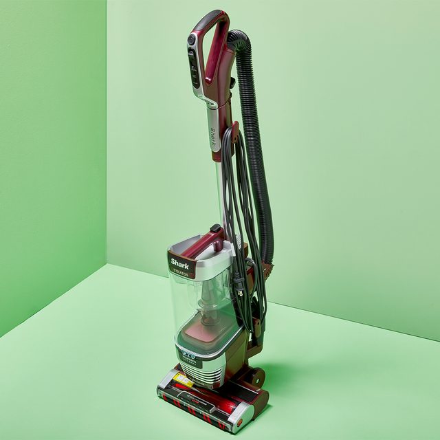 Vacuum cleaner stands upright on a green floor, surrounded by green walls. The brand 