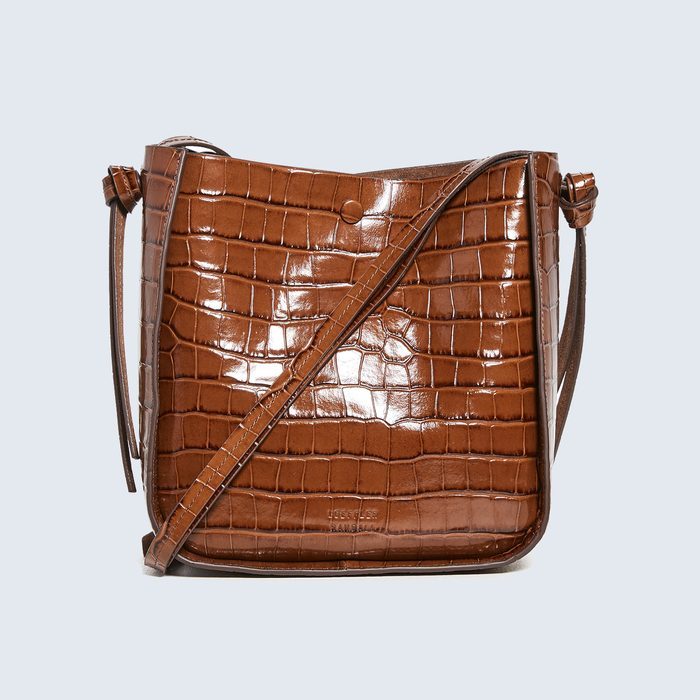 Brown textured handbag sits upright, featuring a glossy crocodile pattern with a long strap, against a plain light background. Text: 