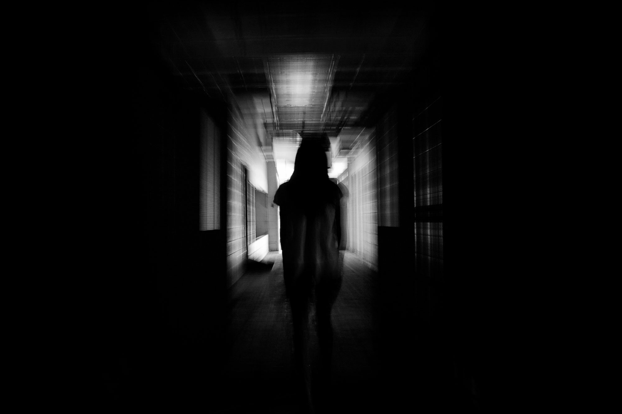 Silhouette walks down a dimly lit, blurry hallway, creating a mysterious and eerie atmosphere.