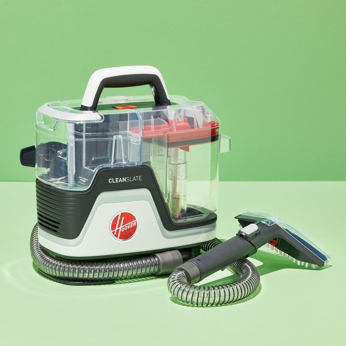 Cleaning machine stands static, surrounded by a coiled hose in a bright green room. Visible text: 