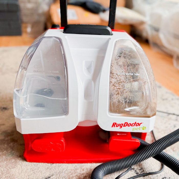 Carpet cleaner sits on a rug, featuring clear and waste water tanks; labeled 