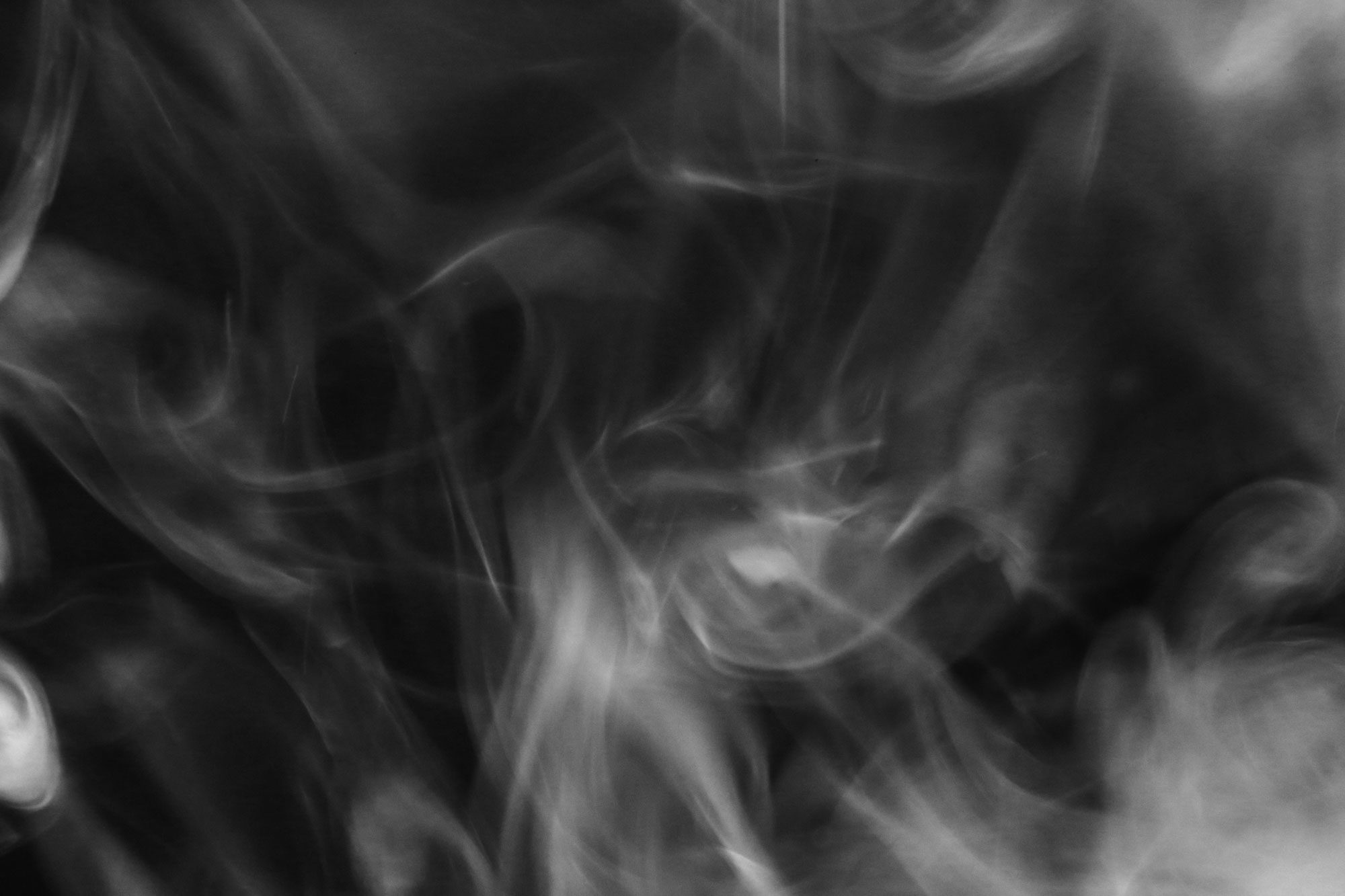 White smoke swirls intricately against a dark background, creating abstract patterns and a mysterious atmosphere.