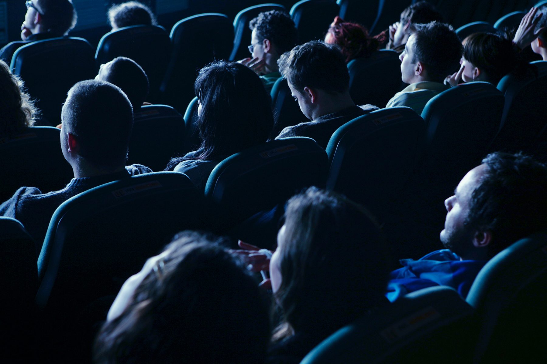 People seated, watching screen in dimly lit theater.