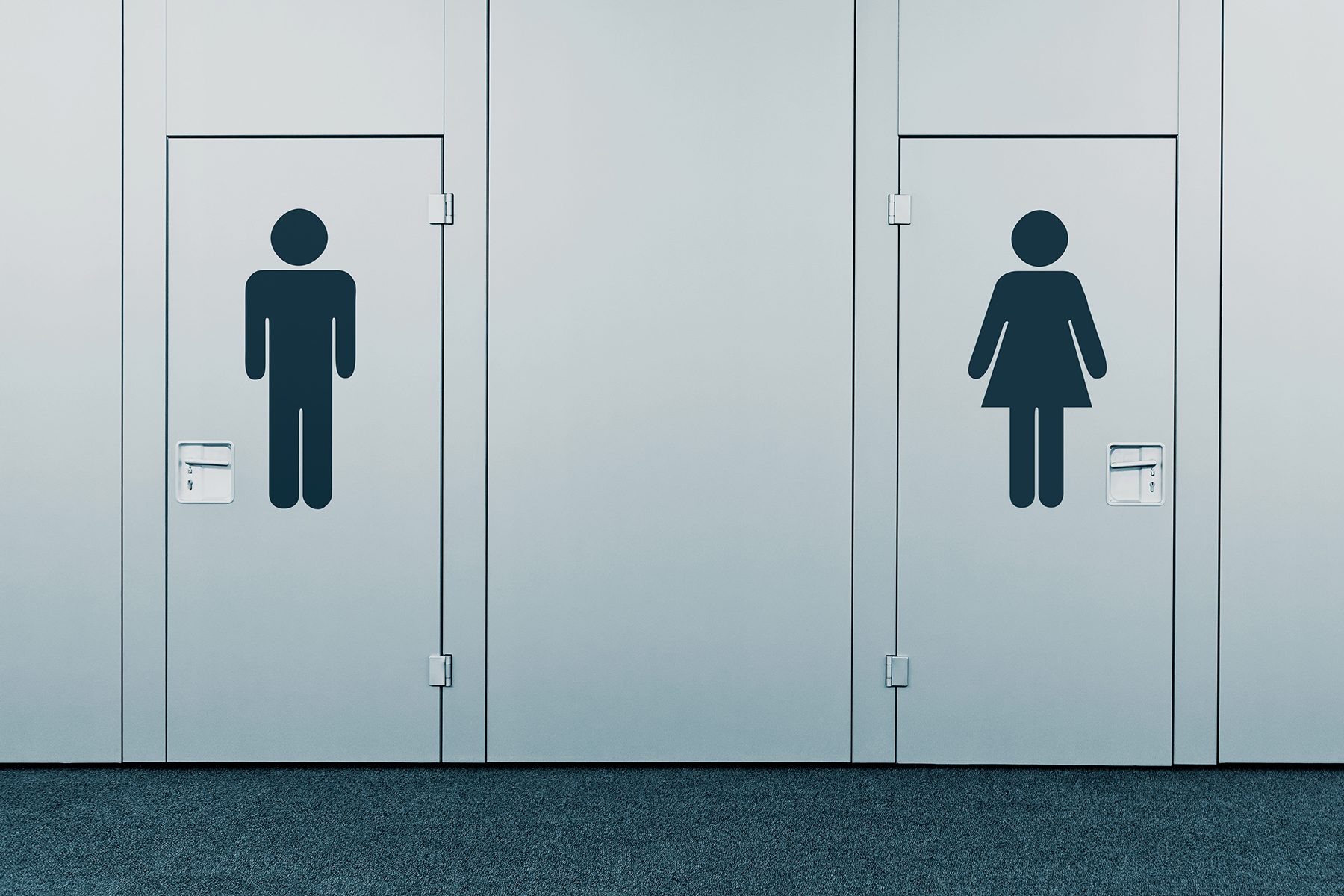 Two restroom doors, each with a gender symbol, are closed in a hallway with a carpeted floor.