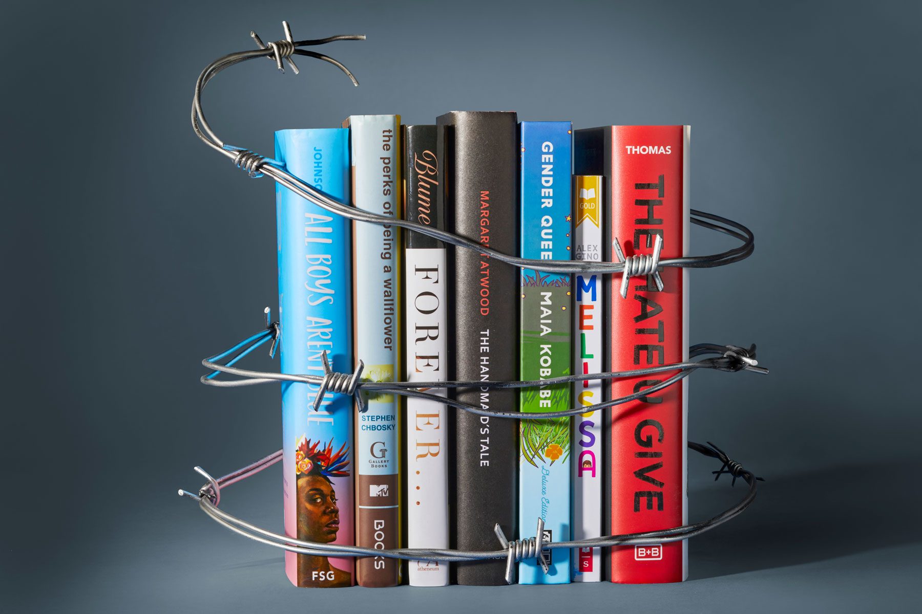 Books are encircled by barbed wire, suggesting restriction or censorship, set against a plain gray background.