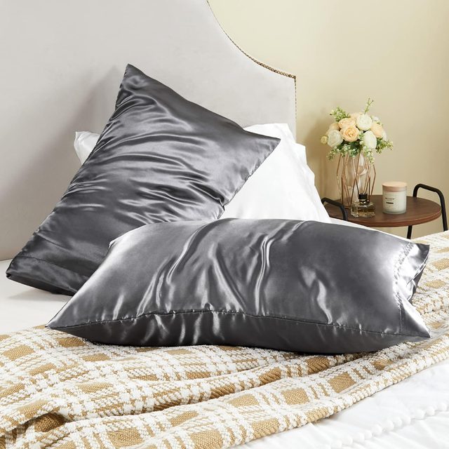 Satin pillows rest on a bed; one is upright, others lay flat. A side table with flowers and a candle completes the serene setting.