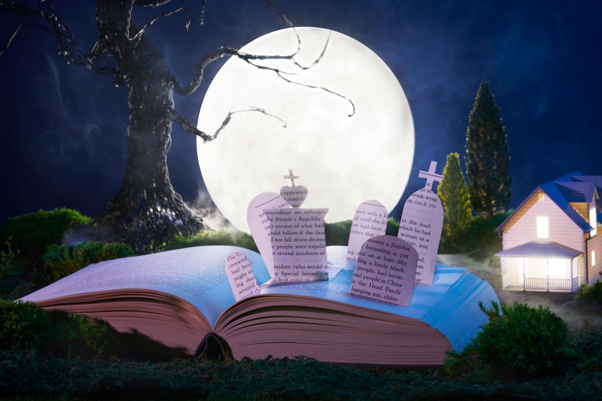 An open book forms a graveyard scene, with paper tombstones under a full moon beside a lit house, surrounded by eerie trees and fog.