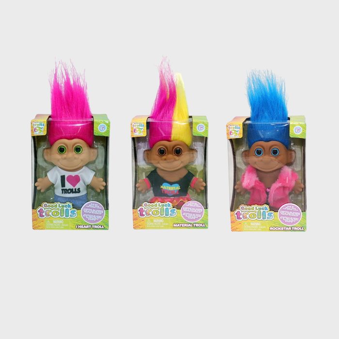 Three troll dolls with vibrant hair stand inside packaging, each wearing a themed outfit. Packaging features text: 