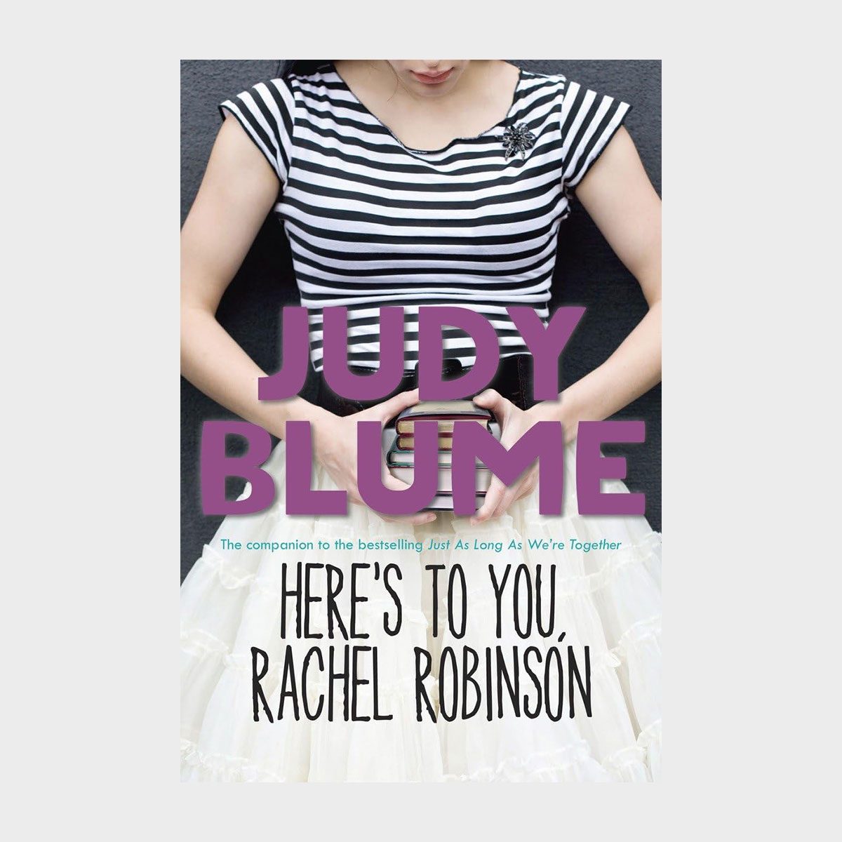 Person holds books against their chest, wearing a striped shirt, layered skirt; text reads "Judy Blume" and "Here's to You, Rachel Robinson."