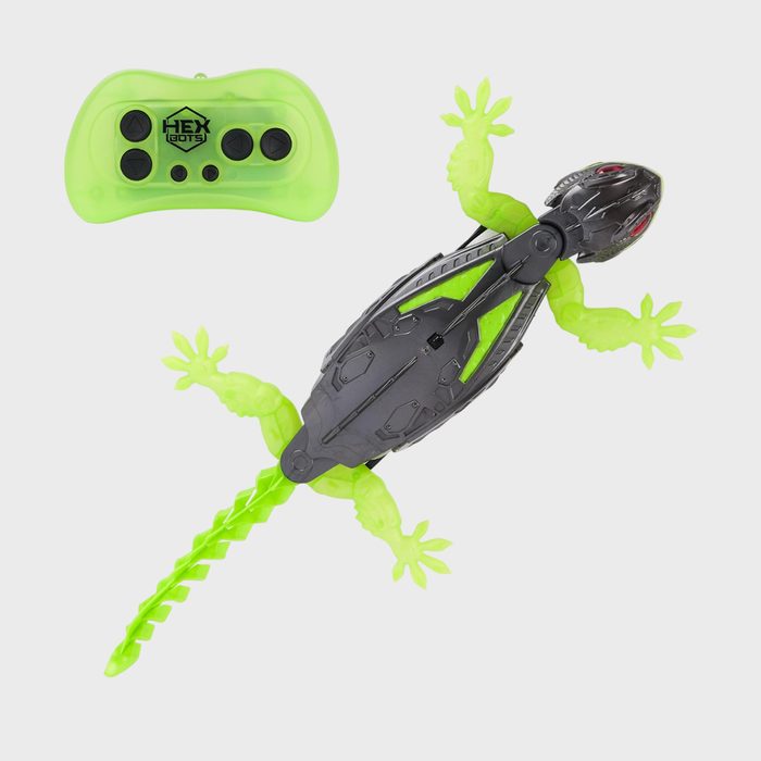 Toy lizard with green limbs lies flat; a neon green remote control is nearby, marked 
