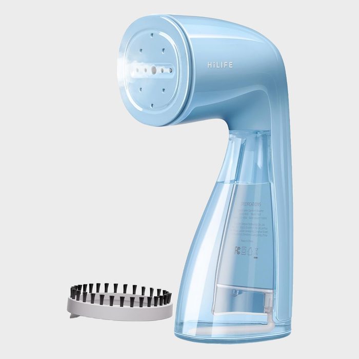 A blue handheld steamer stands upright beside a black bristle attachment on a plain background. The steamer is labeled 