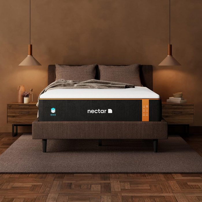 A bed with a Nectar mattress is dressed with a blanket, situated in a cozy bedroom with two nightstands, lamps, and warm lighting.