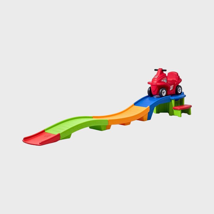 Red toy car sits atop a colorful plastic roller coaster track, with steps leading up, set against a plain background.