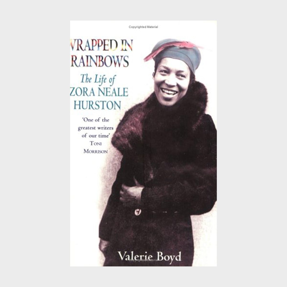 Smiling woman stands, wearing a fur coat and head scarf, on book cover. Text: "Wrapped in Rainbows: The Life of Zora Neale Hurston" by Valerie Boyd.