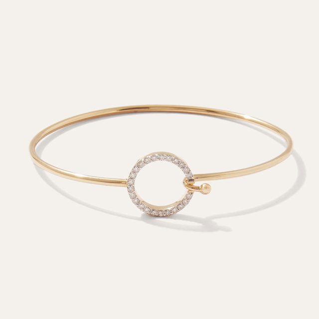 Gold bracelet with a circular clasp adorned with small diamonds, resting on a plain white background.
