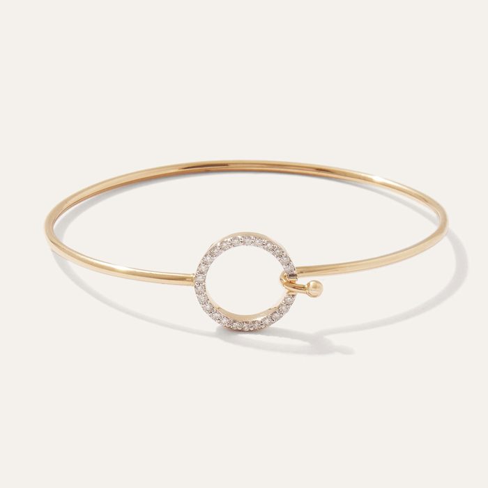 Gold bracelet with a circular clasp adorned with small diamonds, resting on a plain white background.