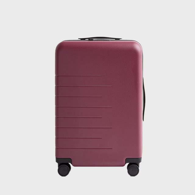 Suitcase stands on four wheels, featuring a burgundy color and horizontal grooves, isolated against a plain white background.