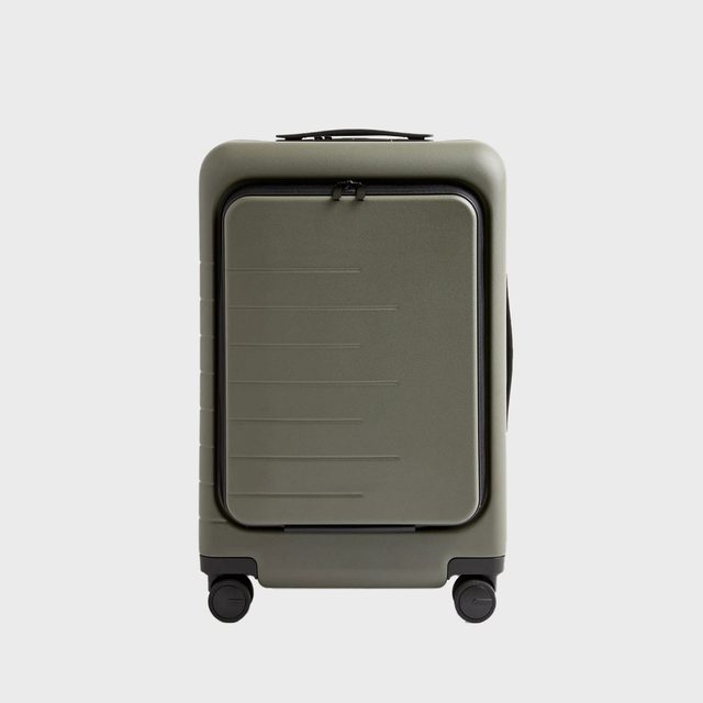 A green suitcase with four wheels stands upright; it has a rectangular design and a handle, set against a plain gray background.