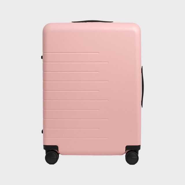 Pink suitcase stands on four wheels; it has horizontal grooves and black handles, set against a plain gray background.