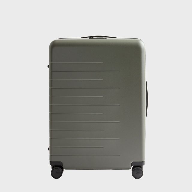 Green suitcase rests on wheels, displaying ridged texture in a minimal studio setting.