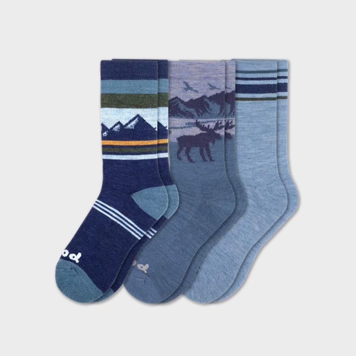 Three pairs of patterned socks lie side by side, featuring mountain designs, moose silhouettes, and stripes, set against a plain white background.