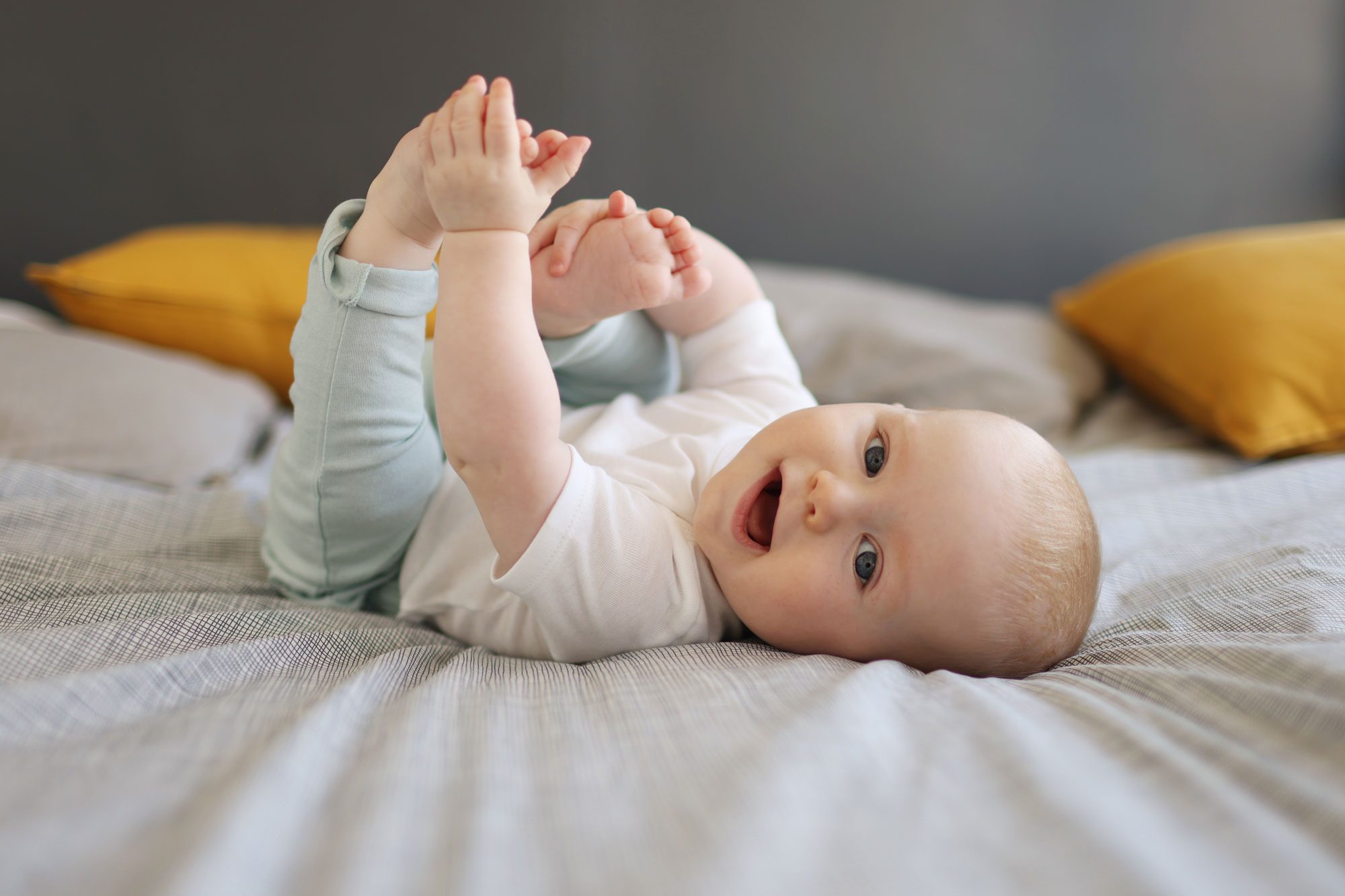 A 6 Month Old Baby Boy Smiling Laying On A Bed