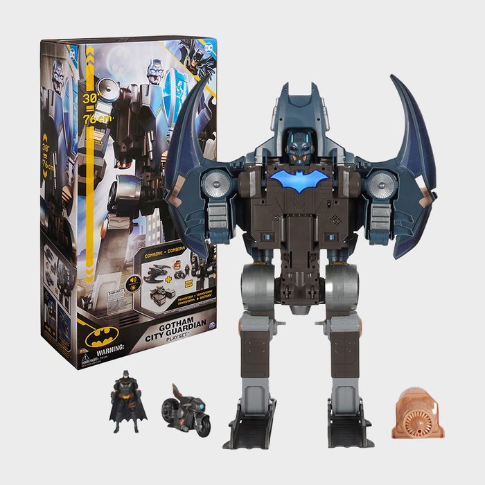 Robot toy stands upright with raised arms, surrounded by packaging and small action figures. Text includes â€œGOTHAM CITY GUARDIAN PLAYSETâ€ and warnings.