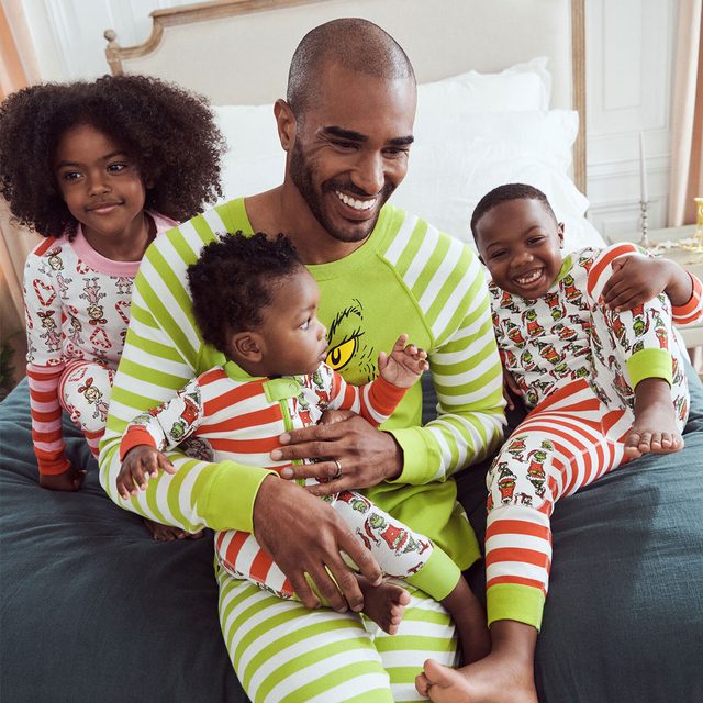 Children wearing colorful pajamas sit and smile with a man on a bed, creating a joyful family moment indoors.