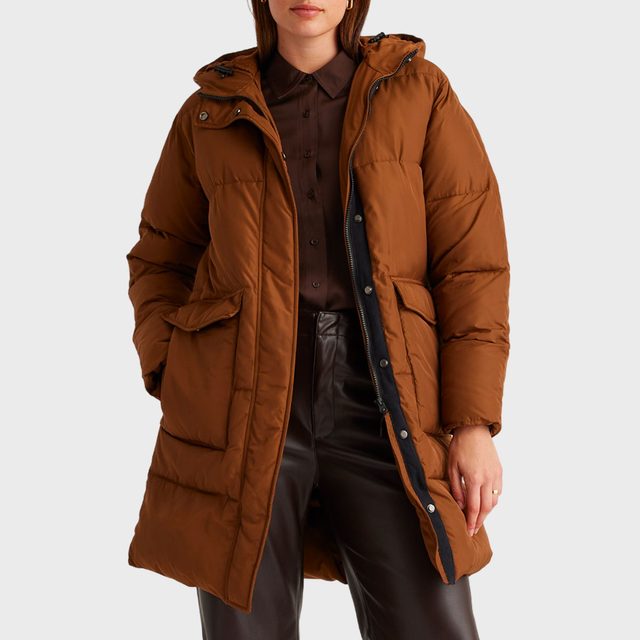 A person wears a brown quilted coat over a brown shirt and dark pants, standing against a plain white background.