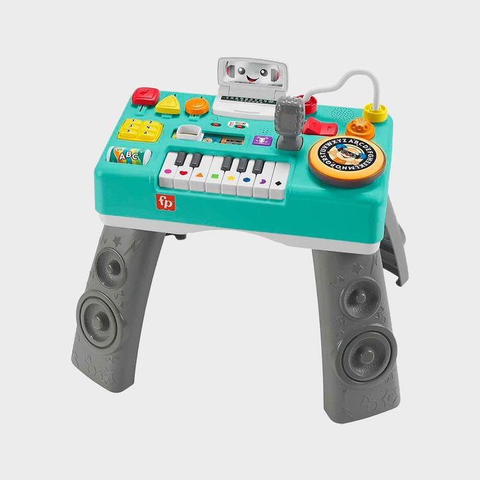 Toy musical activity table featuring piano keys, colorful buttons, and dials, resting on speaker-embellished legs in a white studio setting.