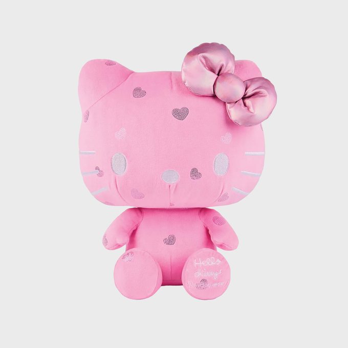 A pink plush cat sits adorned with sparkly hearts and a shiny bow, on a plain background. Text on the paw reads, 